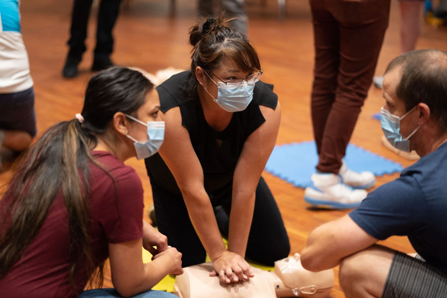 A group of young adults practicing CPR on an adult size manikin