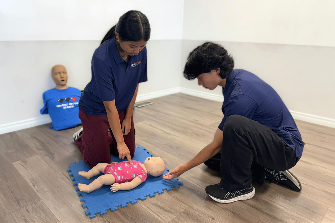 Two people practicing CPR on a mannequin in a classroom setting.