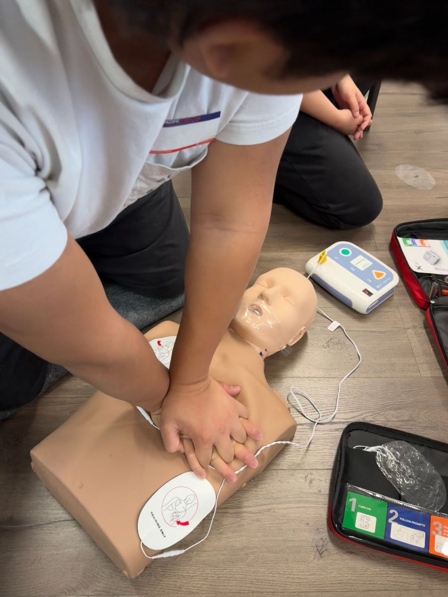 Person performing CPR on a mannequin with AED equipment nearby