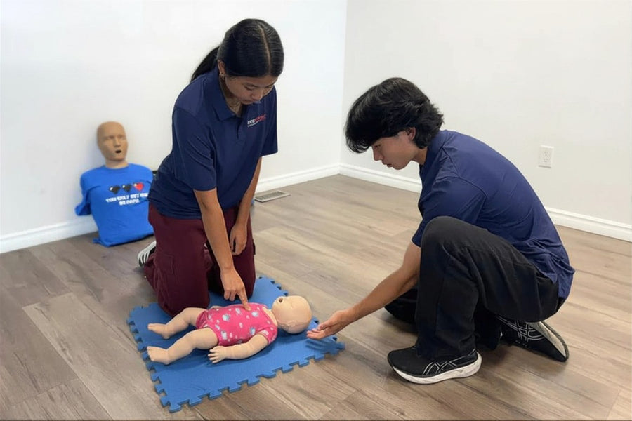 Two people practicing CPR on a mannequin in a classroom setting.
